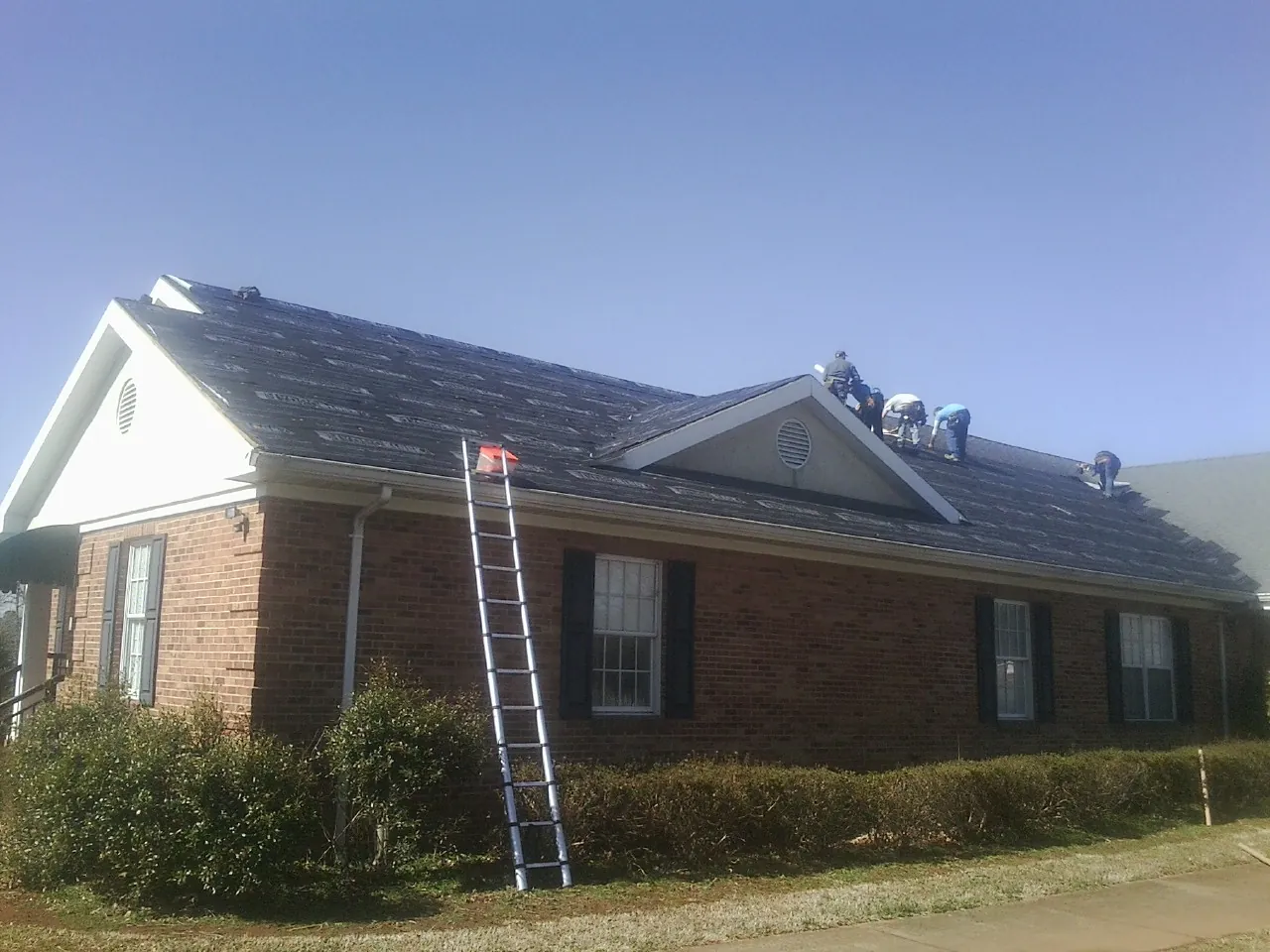 Crew tearing shingles off a brick ranch roof with a ladder set — Emergency Roof Repair work by our crew in Largo
