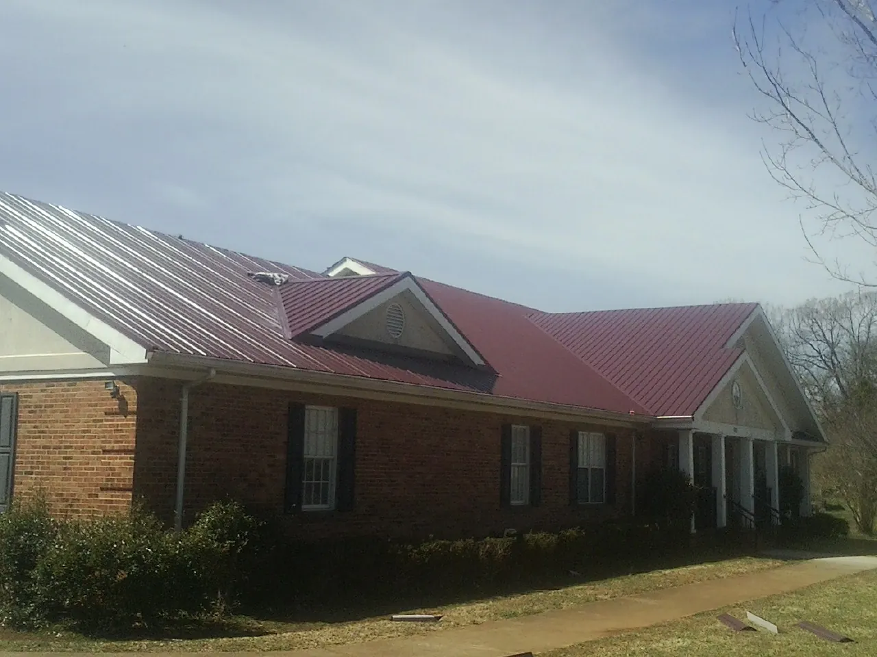 Red metal roof with gabled entries on a long brick building, from a Hail Damage Roof Repair job in Largo