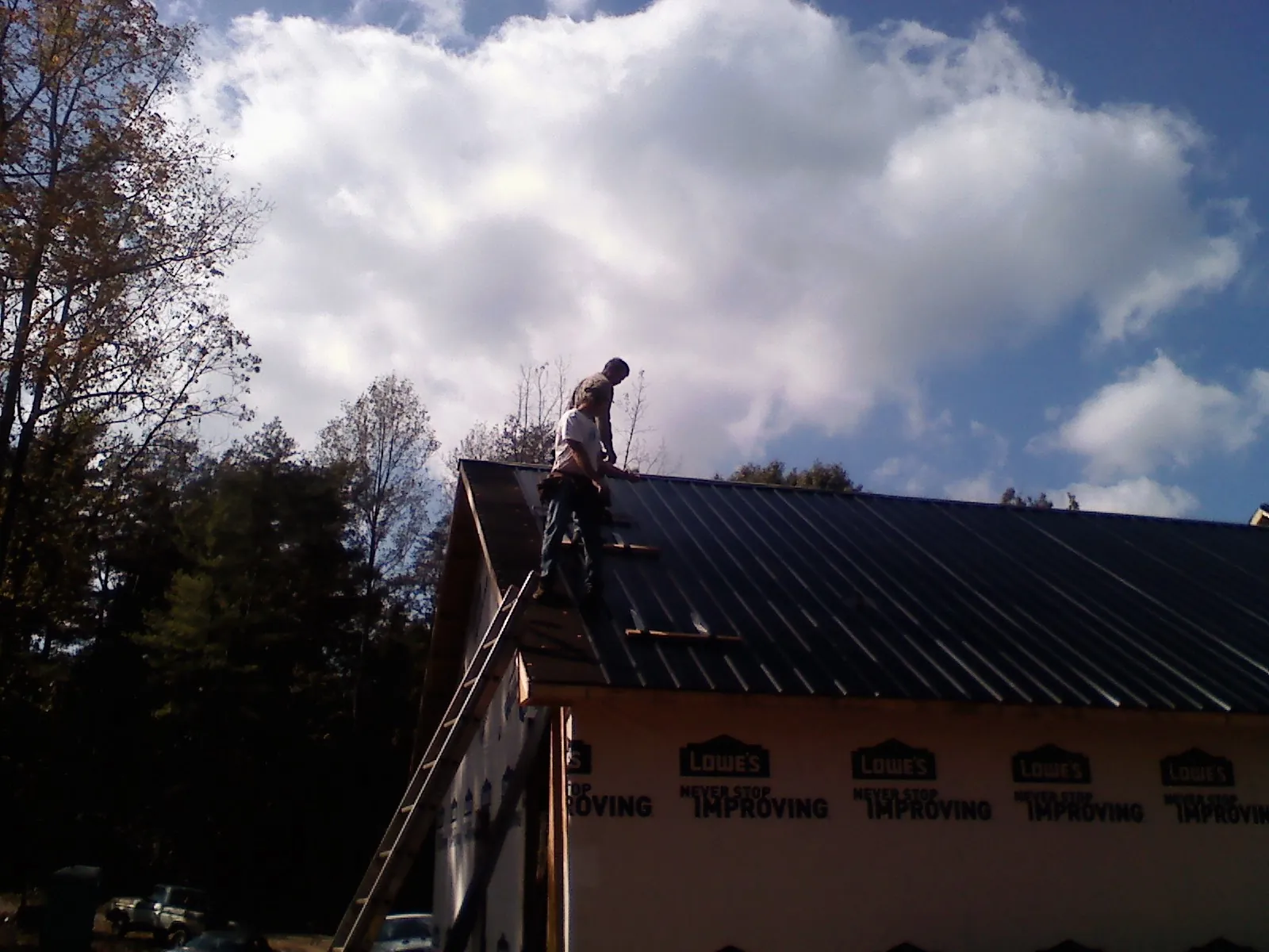 Roofer fastening dark metal panels high against a cloudy sky, from a Roof Inspection job in Largo